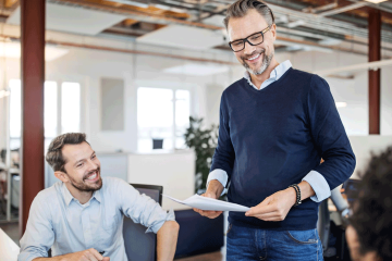 Mature businessman holding a document talking with colleagues sitting in office. Team having meeting over new business plan in the office