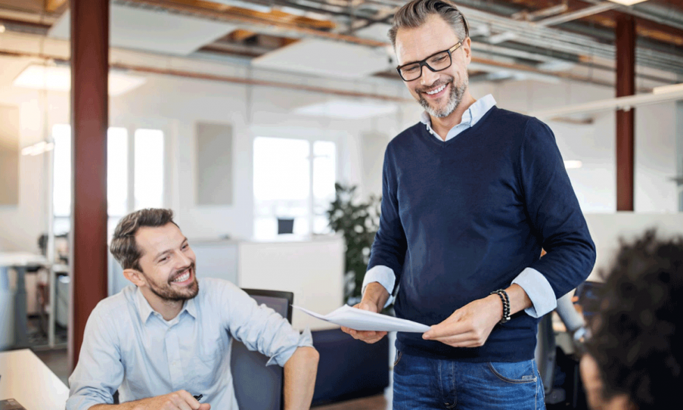 Mature businessman holding a document talking with colleagues sitting in office. Team having meeting over new business plan in the office